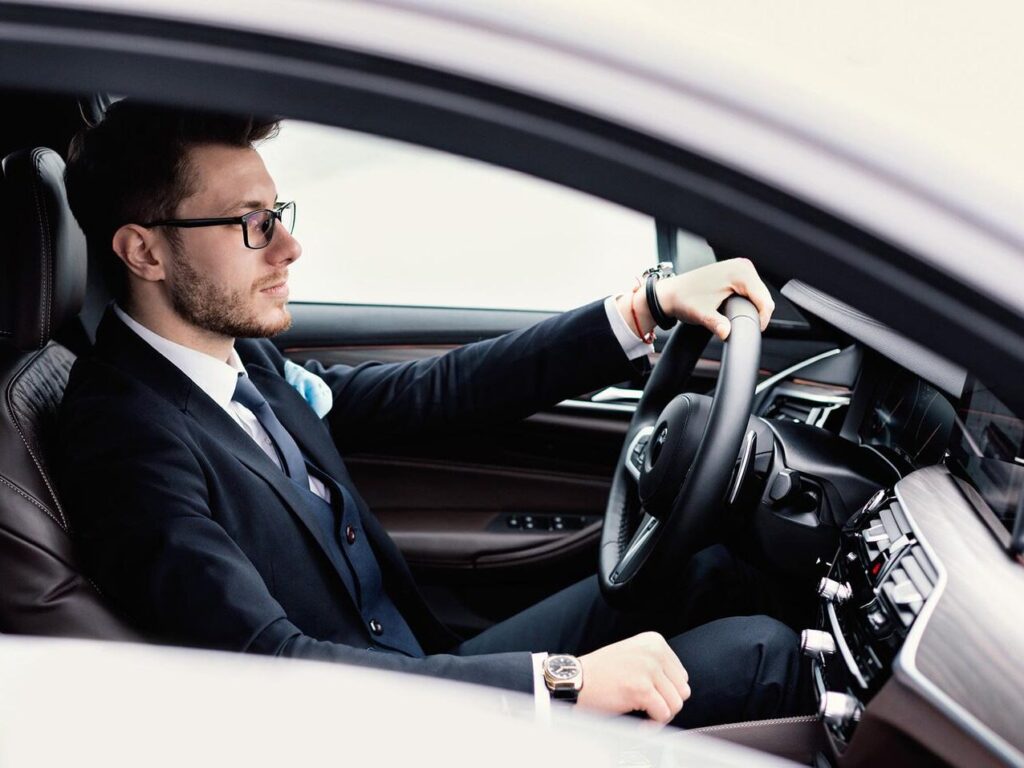 Confident Businessman Concept. Young man in glasses driving in luxury car, side view
